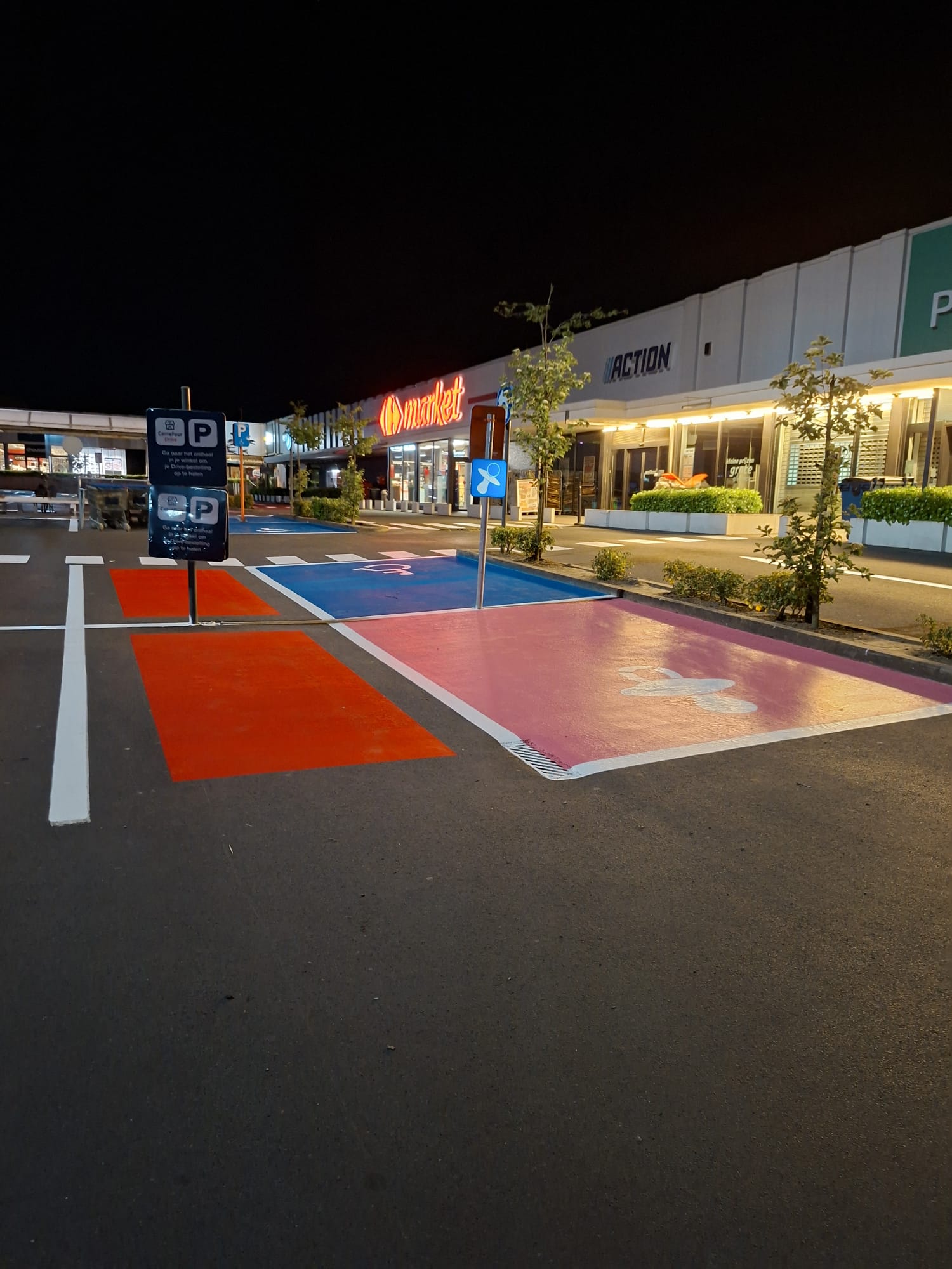 Kleurrijke parkeerzones (rood, blauw, roze) bij Carrefour Market en Action — nachtwerk door Mari-Lines